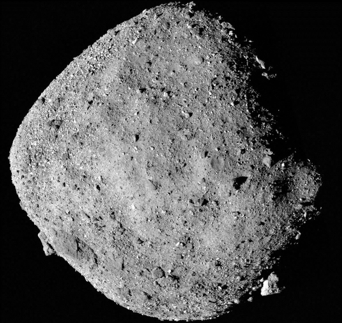 Ein grauer, unregelmäßig geformter Asteroid mit einer rauen, felsigen Oberfläche, die mit kleinen Kratern und Steinen übersät ist, schwebt im Weltraum vor einem schwarzen Hintergrund.