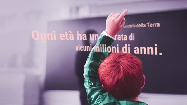 Kleiner Junge meldet sich im Unterricht. An der Tafel steht etwas über die Erdgeschichte in italienischer Sprache.  