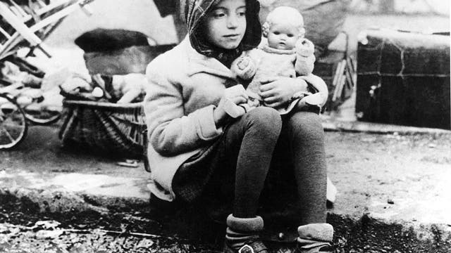 Ein Mädchen, das zu einem Flüchtlingstreck in der Nachkriegszeit gehört, hält seine Puppe im Arm.