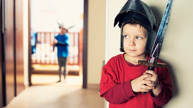 Ein kleiner Junge lauert dem anderen mit einem Spielzeugschwert auf